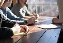 people sitting on chair in front of table while holding pens during daytime